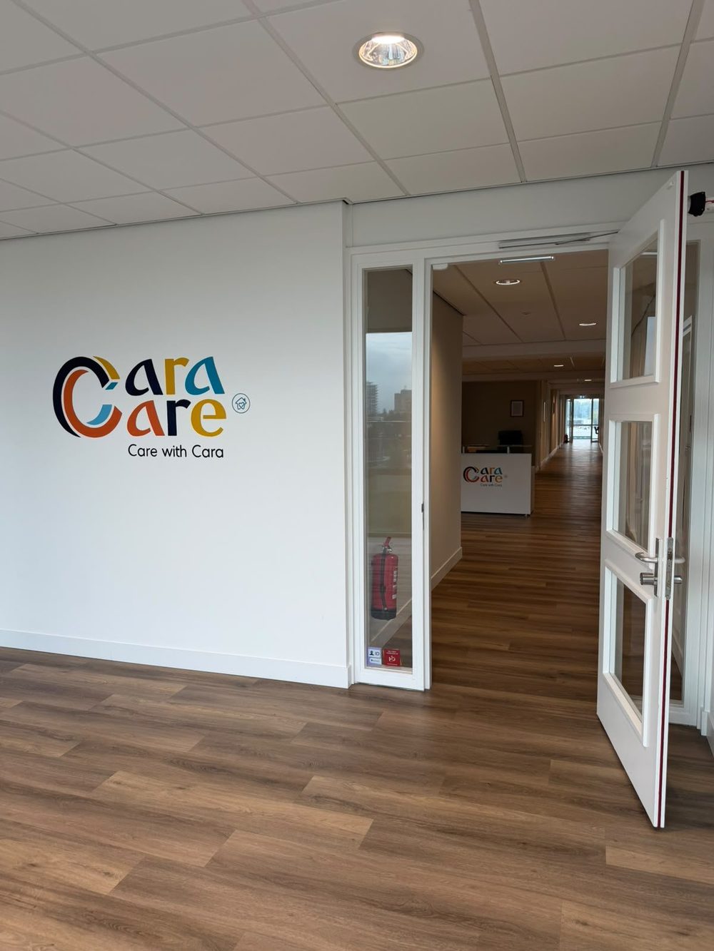 De entree van het kantoor van Cara Care in Schiedam, met het logo op de muur en een openstaande deur